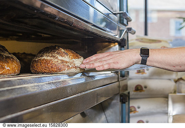 Nahaufnahme einer Hand  die in einen großen  mit Brotlaiben gefüllten Ofen greift
