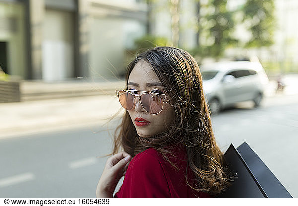 Nahaufnahme einer selbstbewussten Frau mit Sonnenbrille  die eine Einkaufstasche auf einer Straße in der Stadt trägt