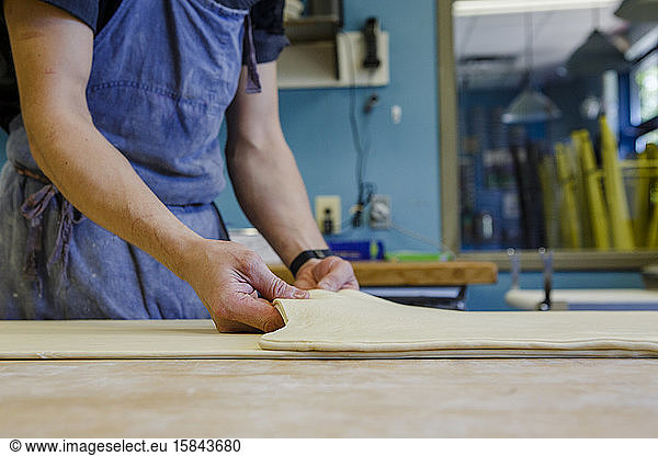 Nahaufnahme eines Bäckers beim Falten von Blätterteig auf bemehlter Oberfläche in der Küche