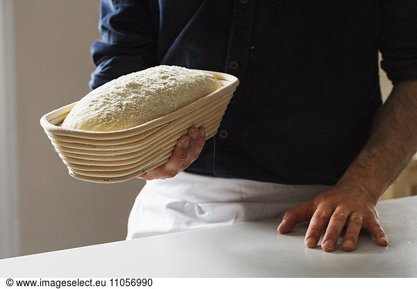 Nahaufnahme eines Bäckers  der einen frisch gebackenen Laib Weißbrot in einem Gärkorb aus Rattan hält.