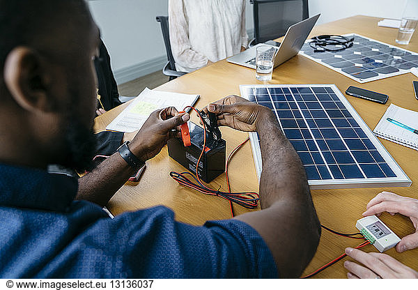 Nahaufnahme eines Geschäftsmannes  der Metallklammern an der Batterie anbringt  während er an einem Solarpanel-Modell arbeitet