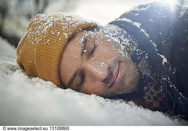 Nahaufnahme eines Mannes  der bei Schneefall auf einer schneebedeckten Motorhaube eines Autos schläft