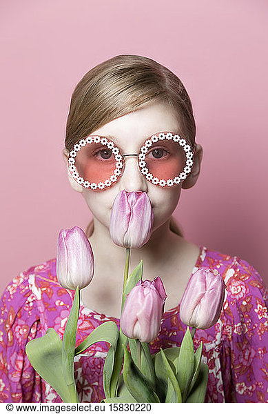Nahaufnahme eines Mod Tween-Mädchens  das an rosa Tulpen auf rosa Hintergrund riecht