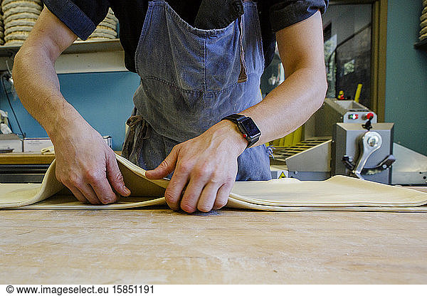 Nahaufnahme eines professionellen Bäckers  der Teig auf bemehlter Oberfläche bearbeitet