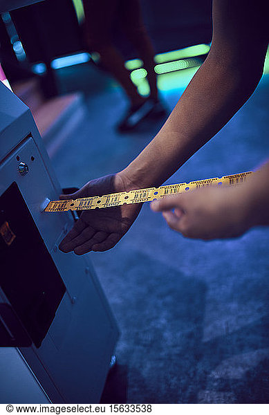 Nahaufnahme eines Teenagers  der in einer Spielhalle Fahrkarten aus einem Automaten nimmt