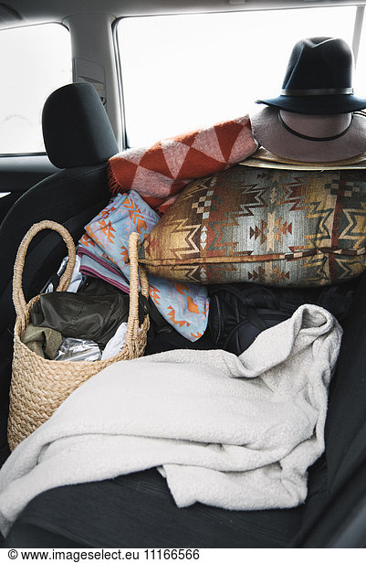 Nahaufnahme von Gegenständen auf dem Rücksitz eines Autos  Kissen  Hüten sowie einer Tasche und einer Decke.