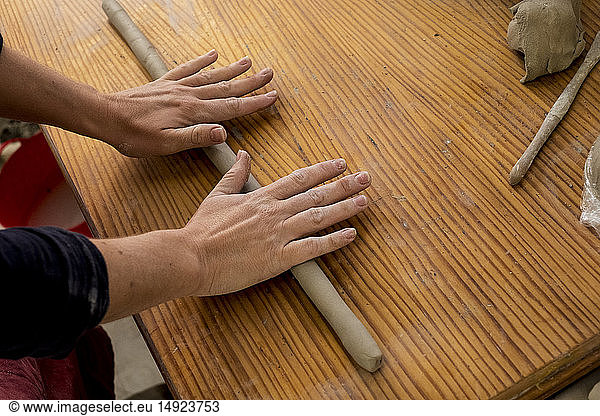 Nahaufnahme von Keramikkünstlerin in ihrem Atelier aus hohem Winkel  wie sie ein Stück Ton auf einem Holztisch ausrollt.