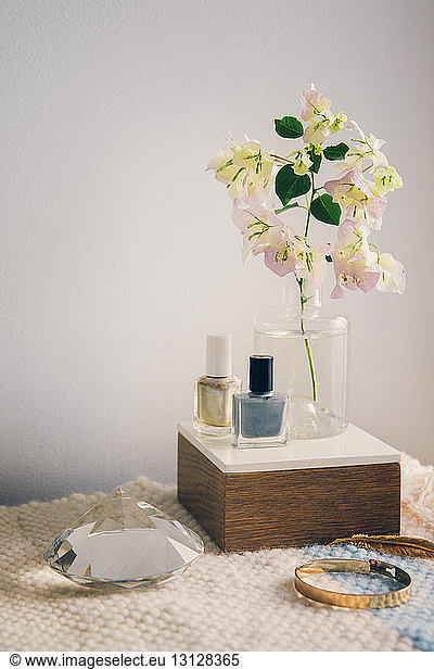 Nail polish with jewelry and crystal by flower vase on table