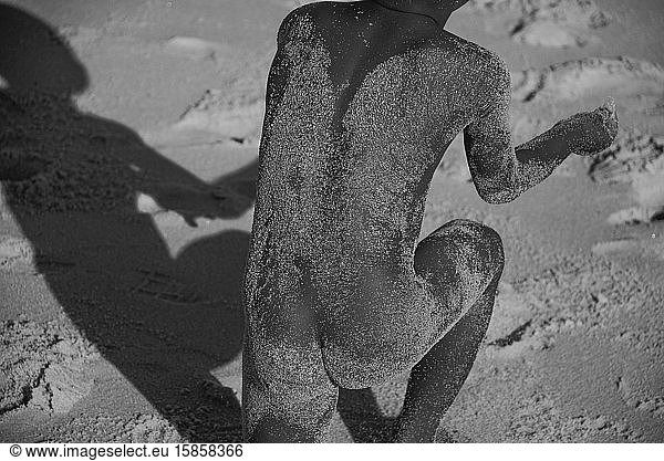 Naked African boy with body full of sand playing in the beach