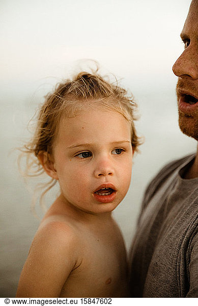 naked curly haired blonde girl with mouth agape is held by her father