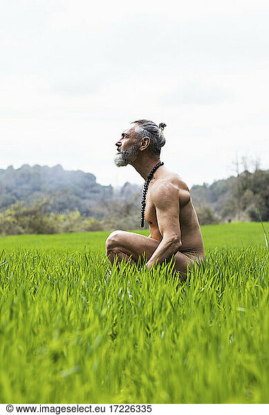 Naked senior man day dreaming while sitting on grass during weekend