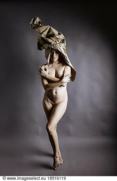 Naked woman wearing paper hat standing on toe