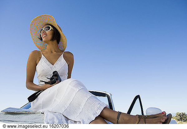 Native American woman in sun dress sitting on white convertible sports car