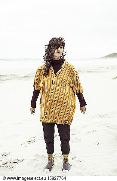 Natural girl stands on windy remote beach with oversized shirt