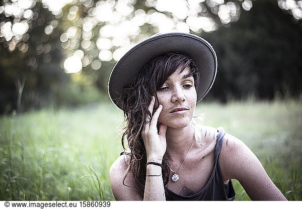 natural girl with freckles and tattoos sits peacefully in long grass