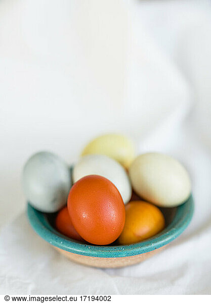 Naturally dyed yellow orange and blue Easter Eggs in a clay bowl