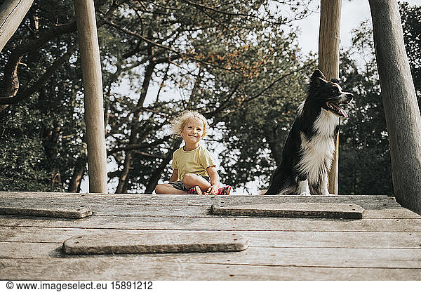 Netherlands  Schiermonnikoog  girl with Border Collie sitting on boardwalk in the forest