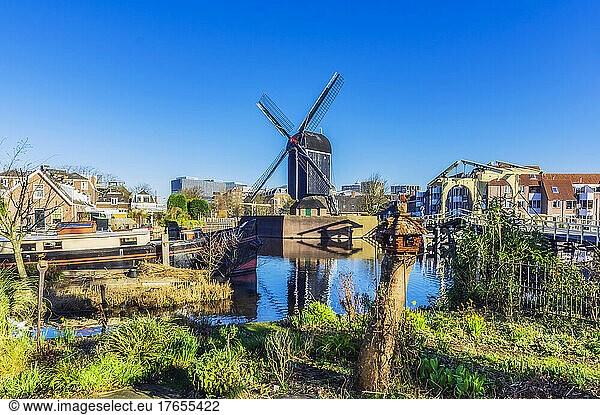 Netherlands  South Holland  Leiden  Clear blue sky over city canal with traditional windmill in background