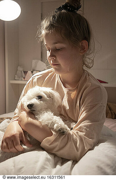 Nettes Mädchen hält Hund im Schlafzimmer sitzend