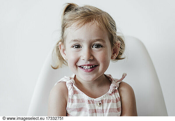 Nettes Mädchen lächelnd auf einem Stuhl sitzend vor einem weißen Hintergrund
