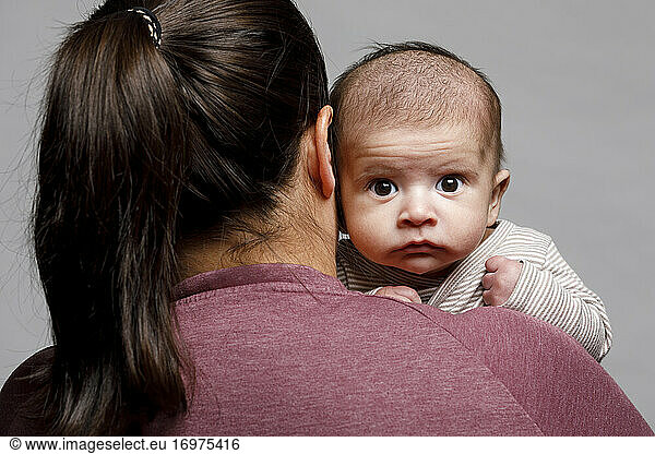 Neugeborenes Baby schaut über die Schulter seiner Mutter und starrt mit großen Augen