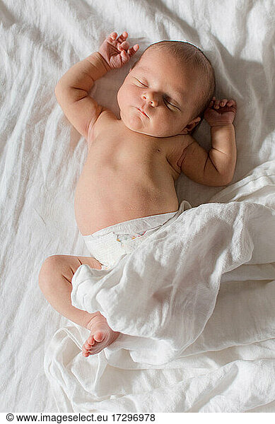 Neugeborenes Baby schläft auf weißem Bett mit weißer Bettwäsche
