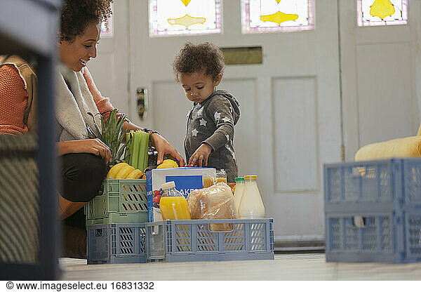 Neugierig Baby Tochter beobachten Mutter auspacken Kiste mit Lebensmitteln