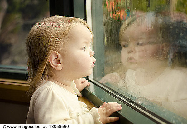 Neugieriges Mädchen schaut durch nasses Fenster