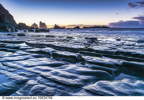 Neuseeland  Südinsel  felsige Meeresküste in der Abenddämmerung mit Motukiekie Beach-Meeresschornsteinen in der Ferne