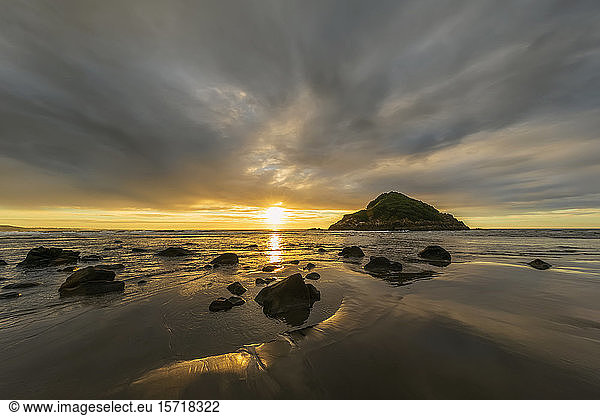Neuseeland  Tongaporutu  Bewölkter Himmel über dem Sandstrand der Küste bei Sonnenuntergang mit der Insel Motuotamatea im Hintergrund