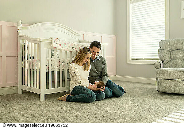 New Parents sitting on baby nursery floor  smiling at baby girl