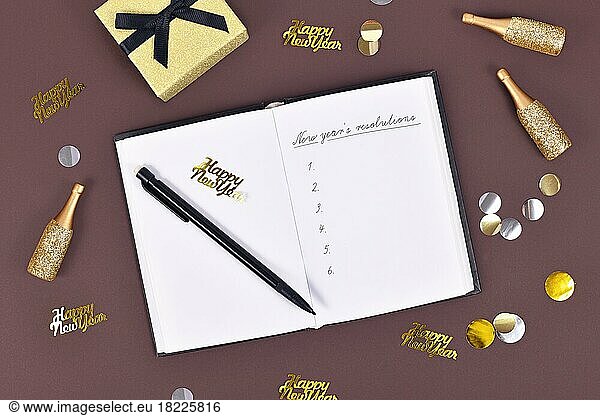 New year's resolutions. Writing a list of plans in open notebook surrounded by New Year party decoration