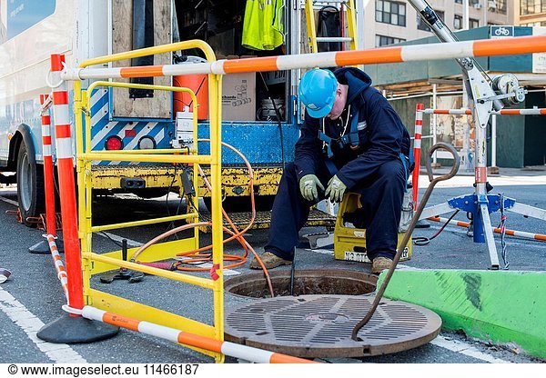 New York City  USA. Caucasian construction worker working above a sewer system manhole on maintaining the tunnels.
