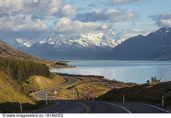 New Zealand  Canterbury Region  Winding asphalt road with Lake Pukaki and Mount Cook in background