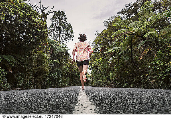New Zealand  North Island  Northland  Young man running on road through Waipoua Forest