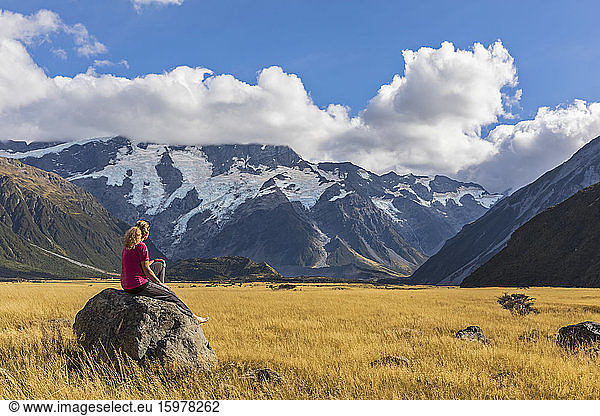 New Zealand  Oceania  South Island  Canterbury  Ben Ohau  Southern Alps (New Zealand Alps)  Mount Cook National Park  Aoraki / Mount Cook  Woman sitting on boulder in mountain landscape