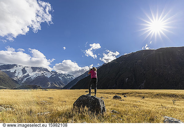 New Zealand  Oceania  South Island  Canterbury  Ben Ohau  Southern Alps (New Zealand Alps)  Mount Cook National Park  Aoraki / Mount Cook  Woman standing on boulder and photographing mountain landscape