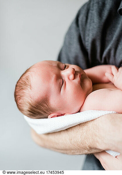 Newborn Baby Boy Held in Father's Arms Neutral Colors with Brown Hair