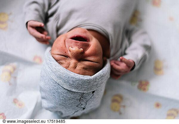 Newborn baby dressed in cap crying disconsolately. Lying on the bed.