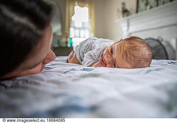 Newborn baby laying on stomach staring at his loving mother.