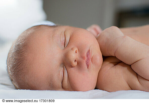 Newborn baby with chubby cheeks and pink lips sleeping on bed.