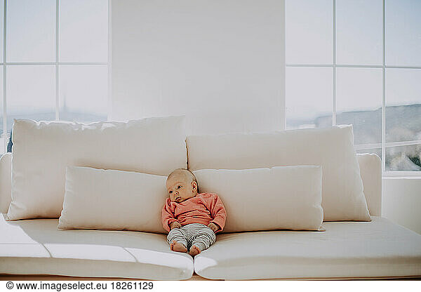 Newborn infant laying on white couch in a white  bright room on