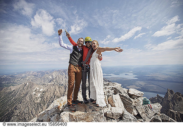 Newlywed bride and groom celebrate with climbing guide on mountaintop