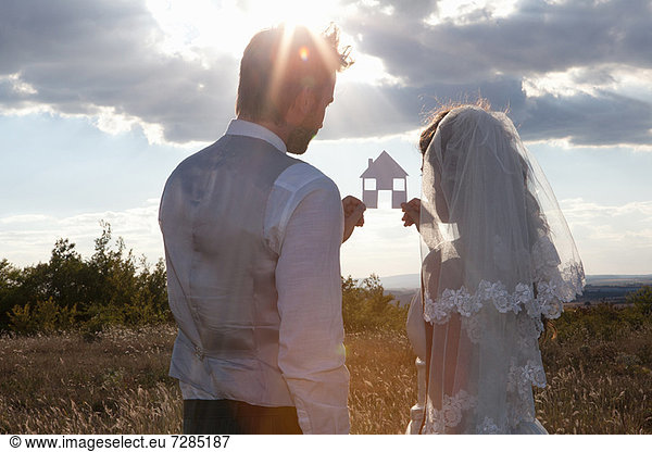 Newlywed couple holding a picture of a house