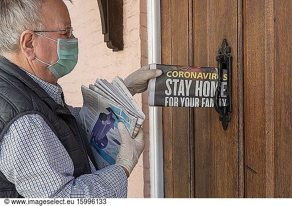 Newspaper delivery man wearing protective mask and surgical gloves while delivering newspapers to a country home  during Coronavirus Pandemic  Hampshire  UK.