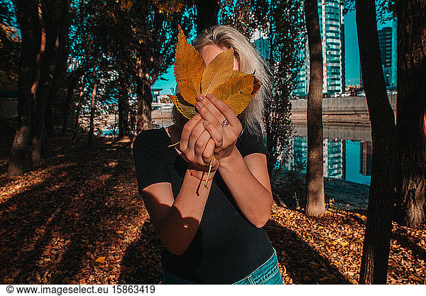 Nice blondi Girl hides behind autumn foliage