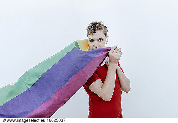Nicht-binäre Person  die eine Regenbogenflagge vor einem weißen Hintergrund hält