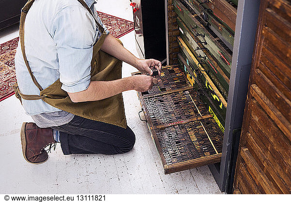 Niederer Teil eines Mannes  der hölzerne Alphabete in einer Schublade an einer Druckerpresse anordnet