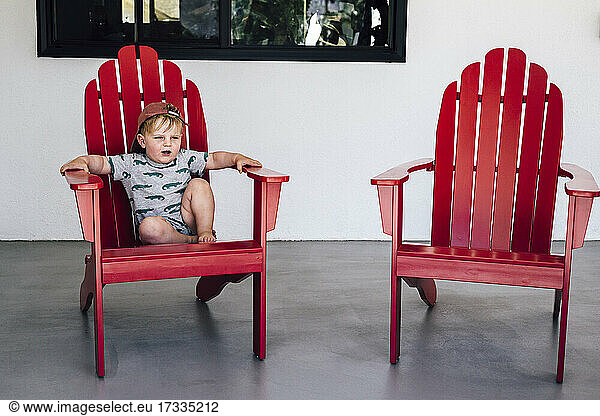 Niedlicher Junge  der auf einem Stuhl im Innenhof sitzt und wegschaut