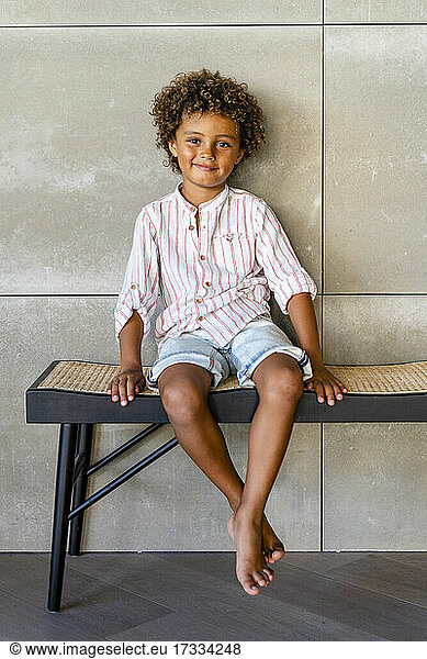 Niedlicher Junge sitzt lächelnd auf einer Bank